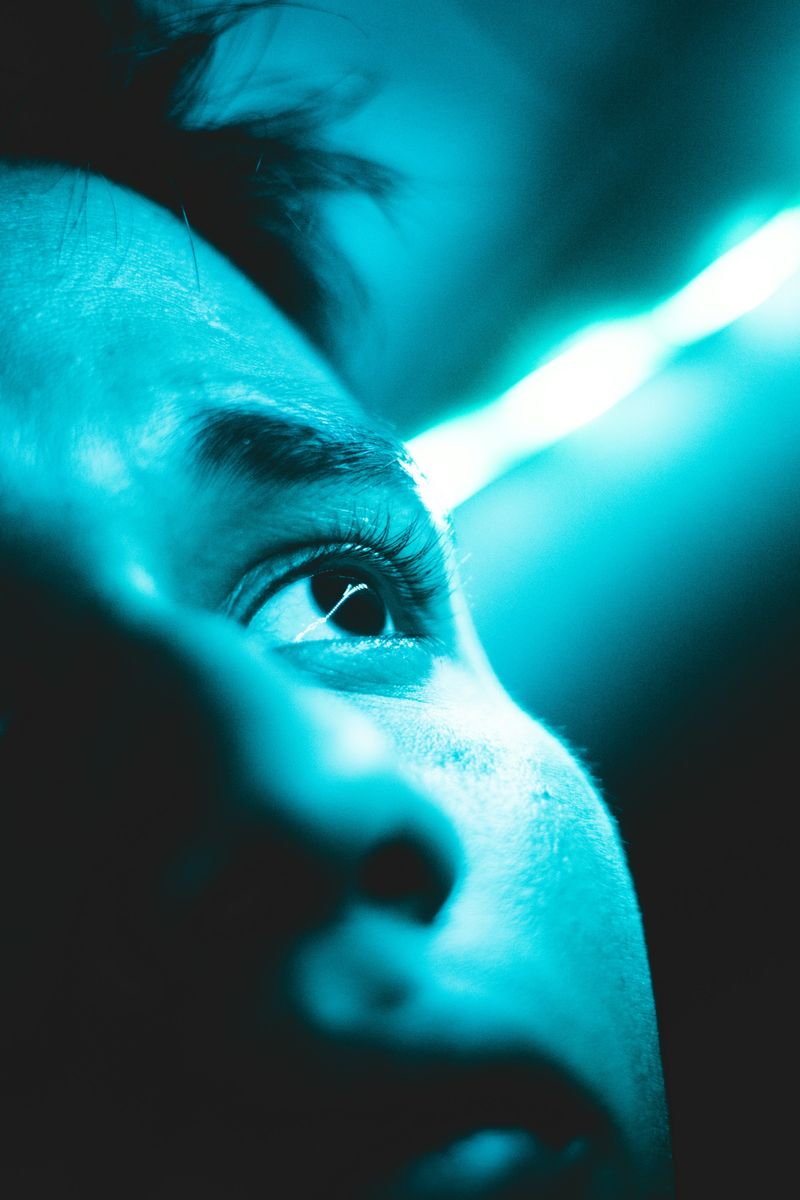 A man's face and eye upclose, under a bright blue teal light.